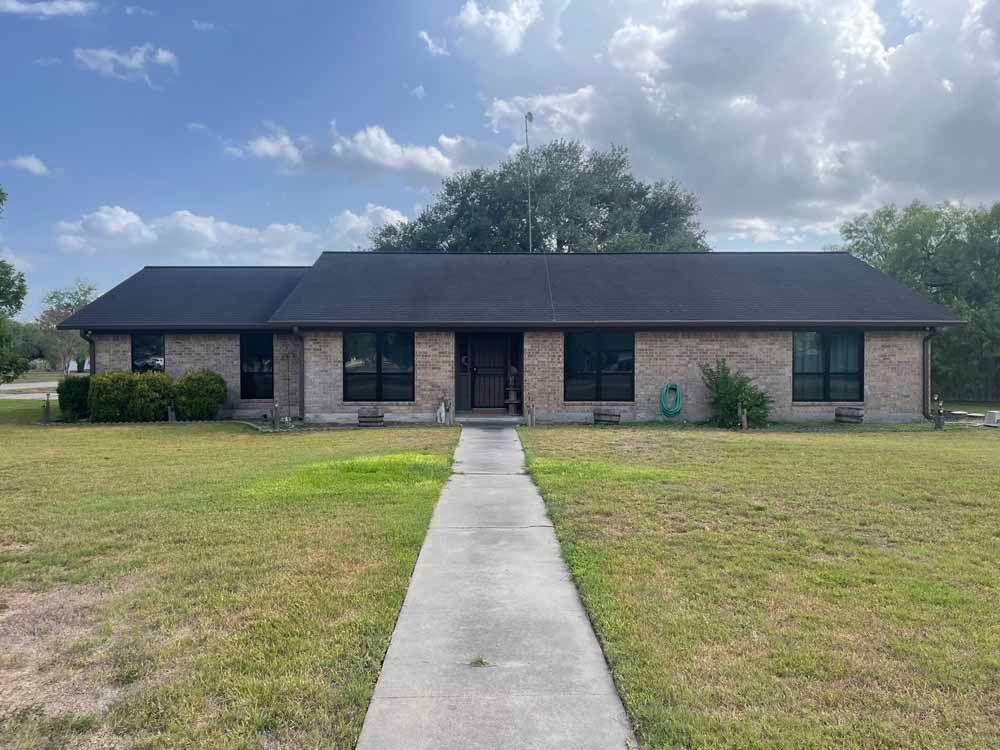 Single-story brick house with a dark roof and a concrete walkway. Overcast sky and green lawn.