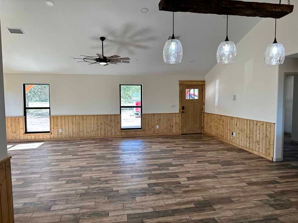 Empty room with wood-look flooring and wainscoting, light-colored walls, windows, and hanging lights.