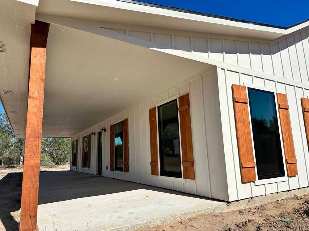 Exterior of a white house with brown shutters and porch beams; clear blue sky.