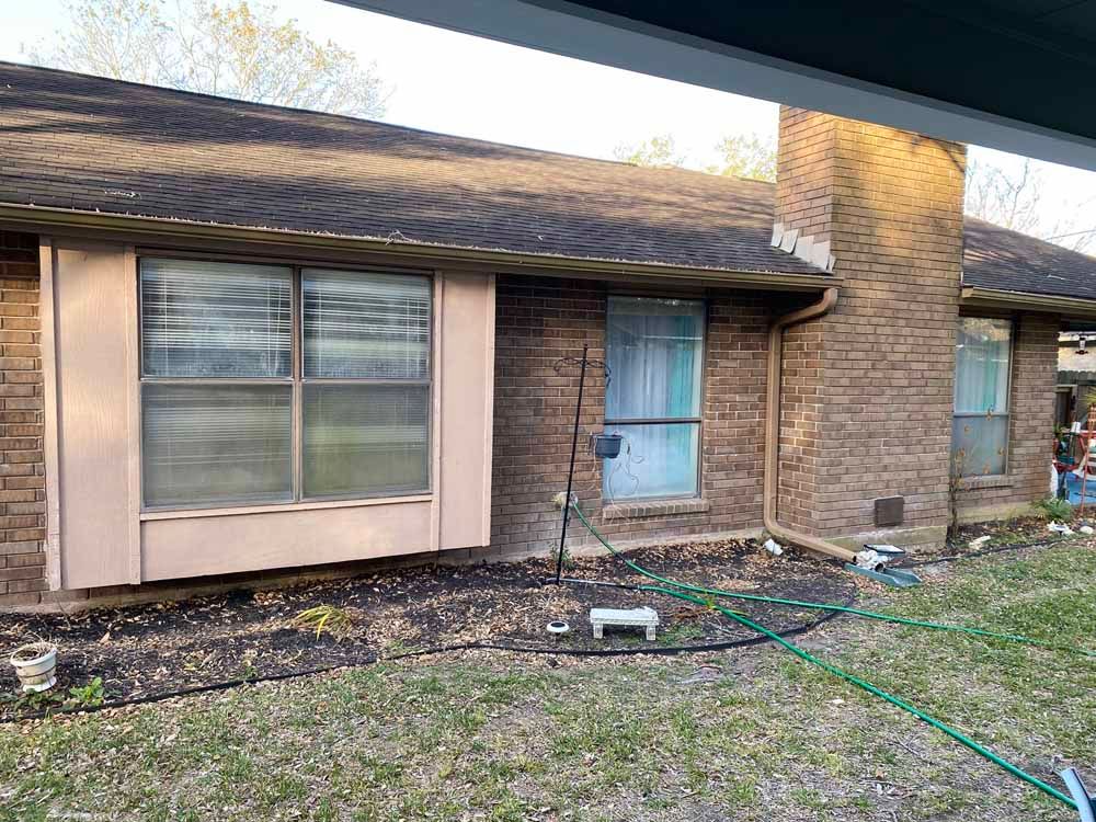 Brick house with windows and a chimney; a garden hose lies in the yard.