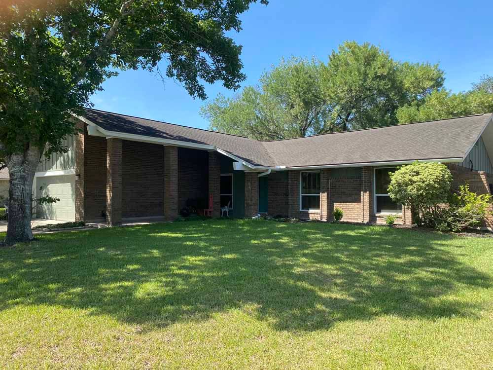 Brick house with a dark roof and green lawn on a sunny day.