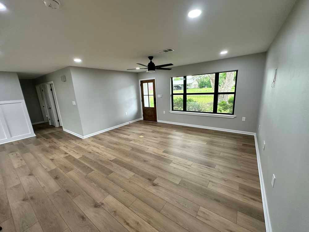 Empty living room with wood flooring, grey walls, door, and windows.