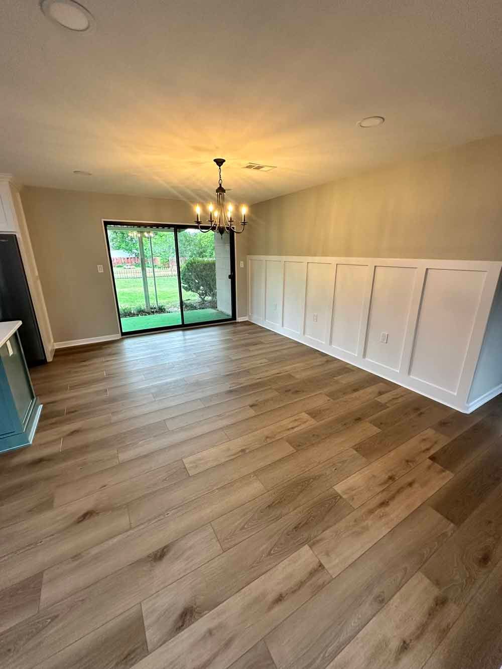 Empty dining room with wood floors, sliding glass door, white wall paneling, and a chandelier.