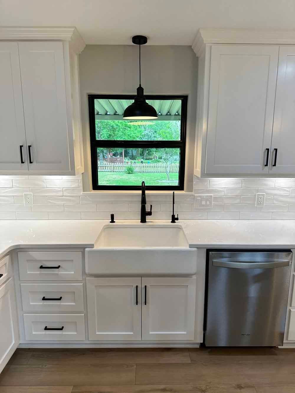 Kitchen with white cabinets, farmhouse sink, black faucet, and a view through a window.