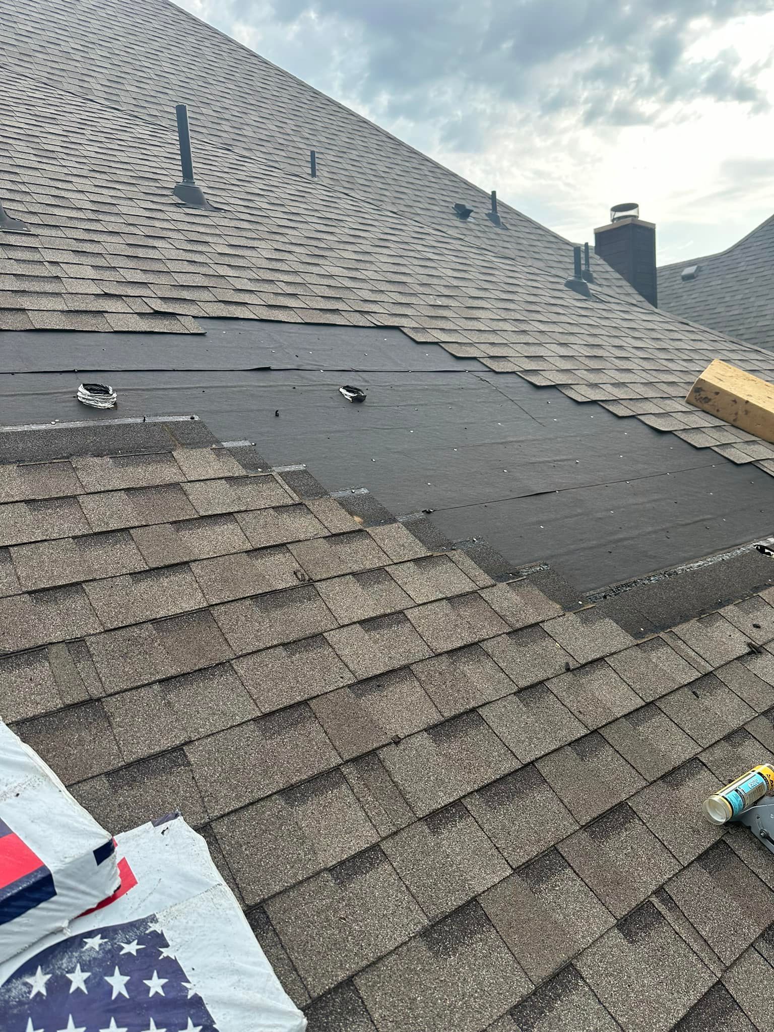 Rooftop with missing shingles, exposing black underlayment. Partially covered, overcast sky.