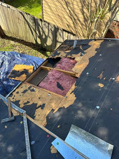 Damaged roof with missing shingles revealing underlying plywood and insulation.