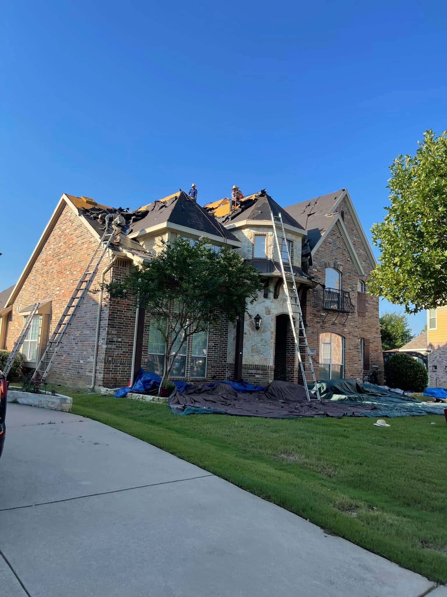 House with fire damage; charred roof and walls, surrounded by debris, ladder propped against structure.