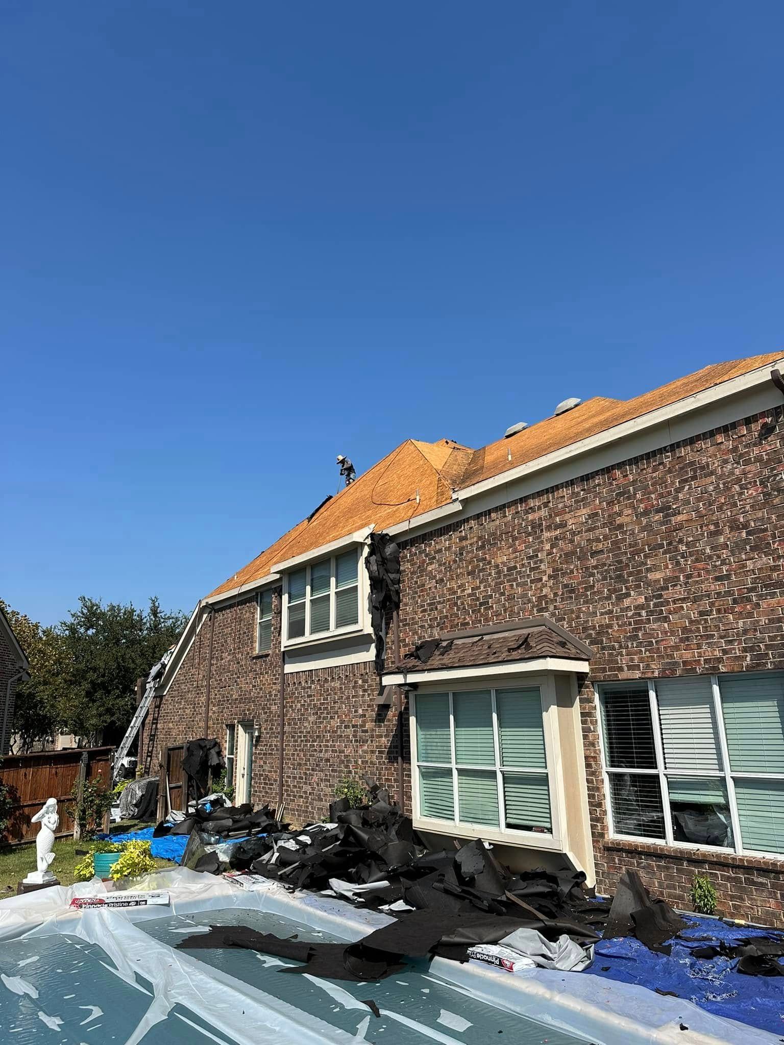 House with damaged roof and debris near a pool on a sunny day.