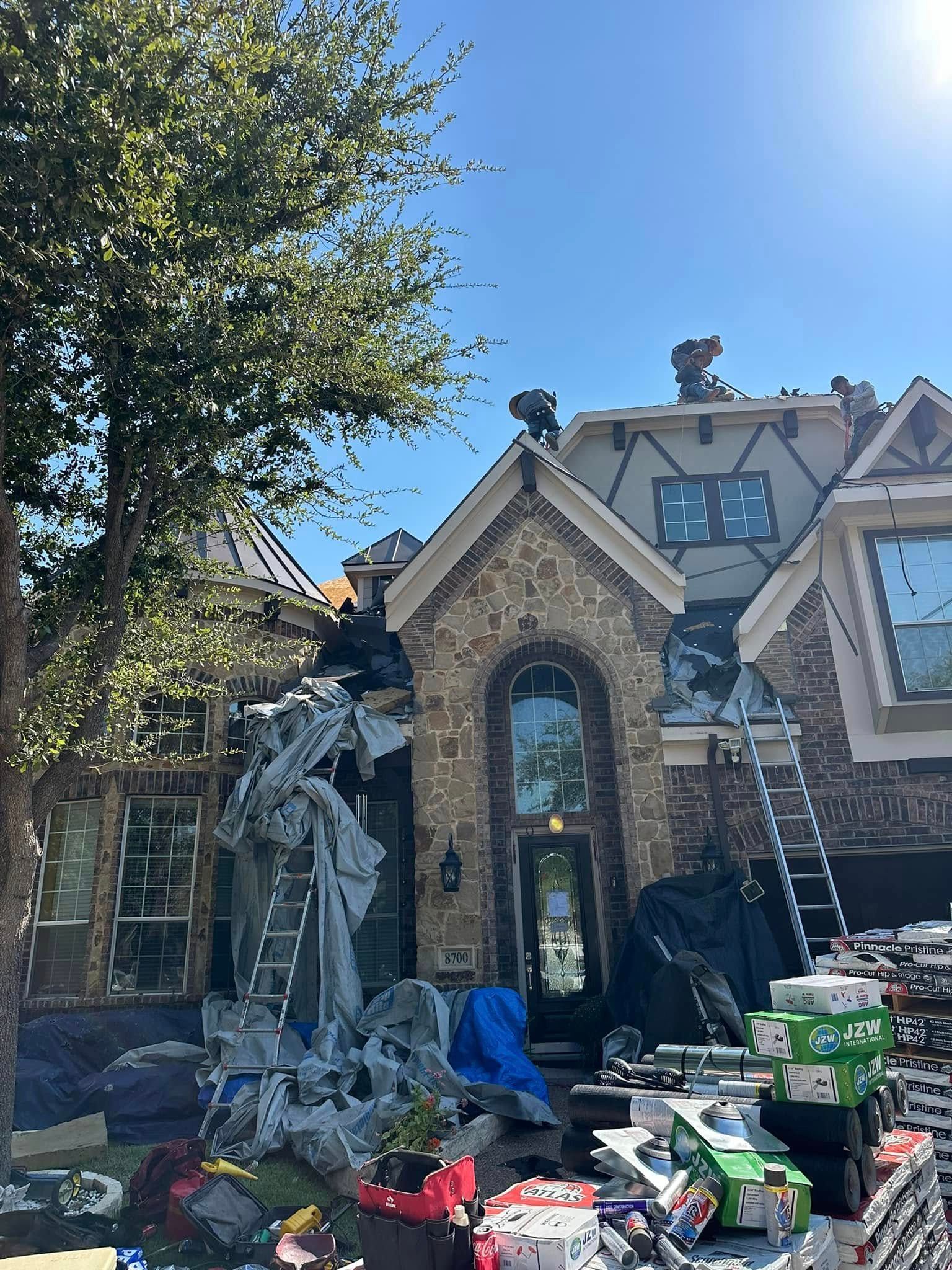 House under construction; brown brick facade, ladders, covered materials, and new shingles on roof.