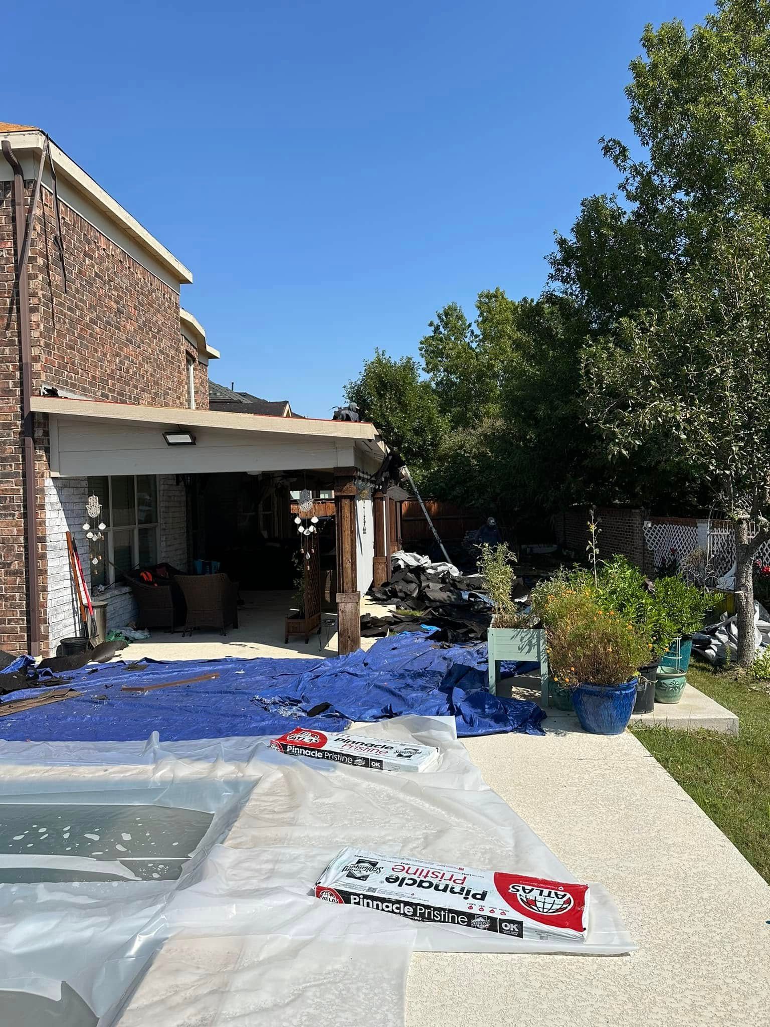 Backyard with scattered blue material, pool, patio, trees, and a two-story brick house on a sunny day.