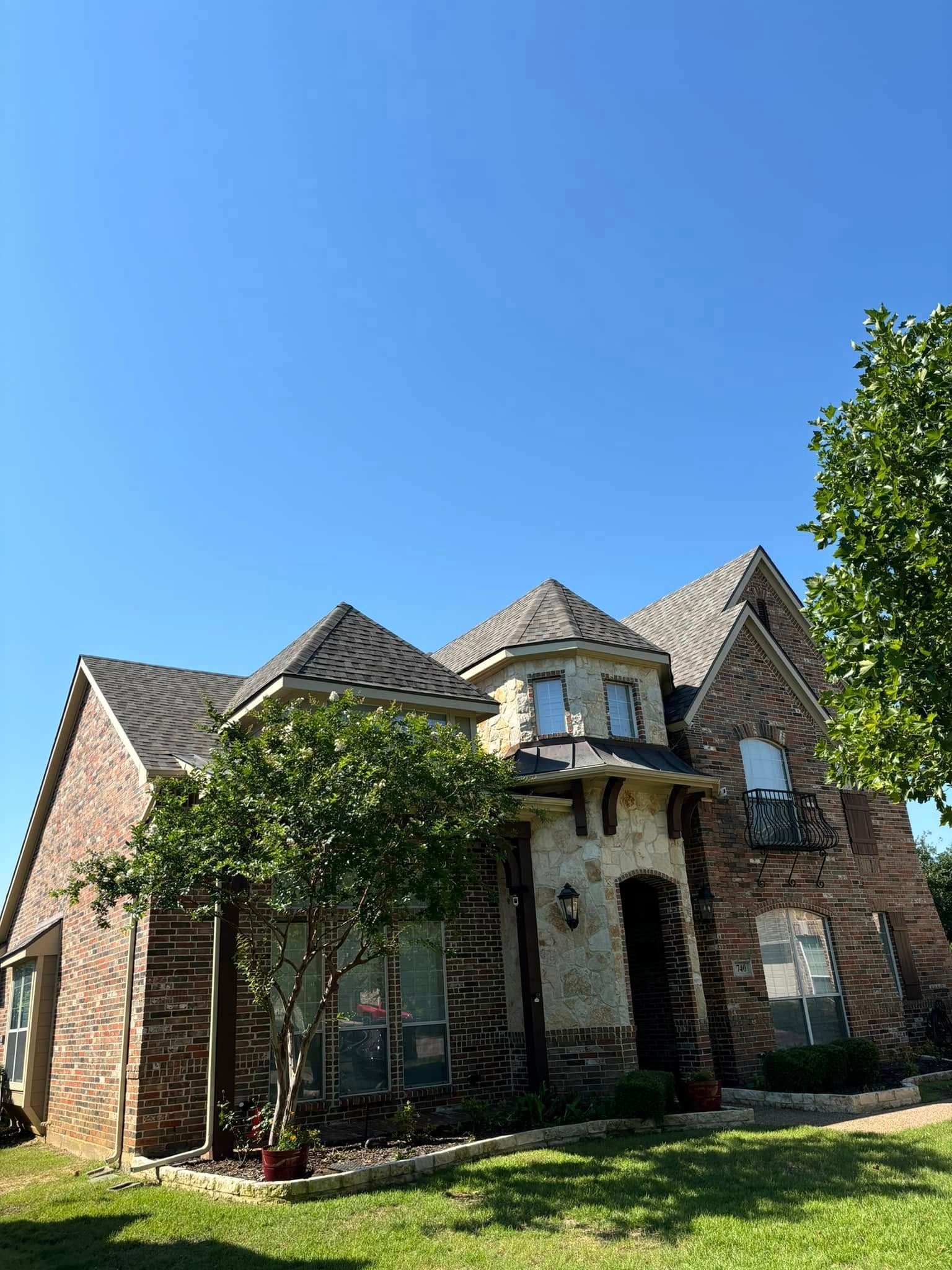 Brick house with a turret, green lawn, and blue sky.