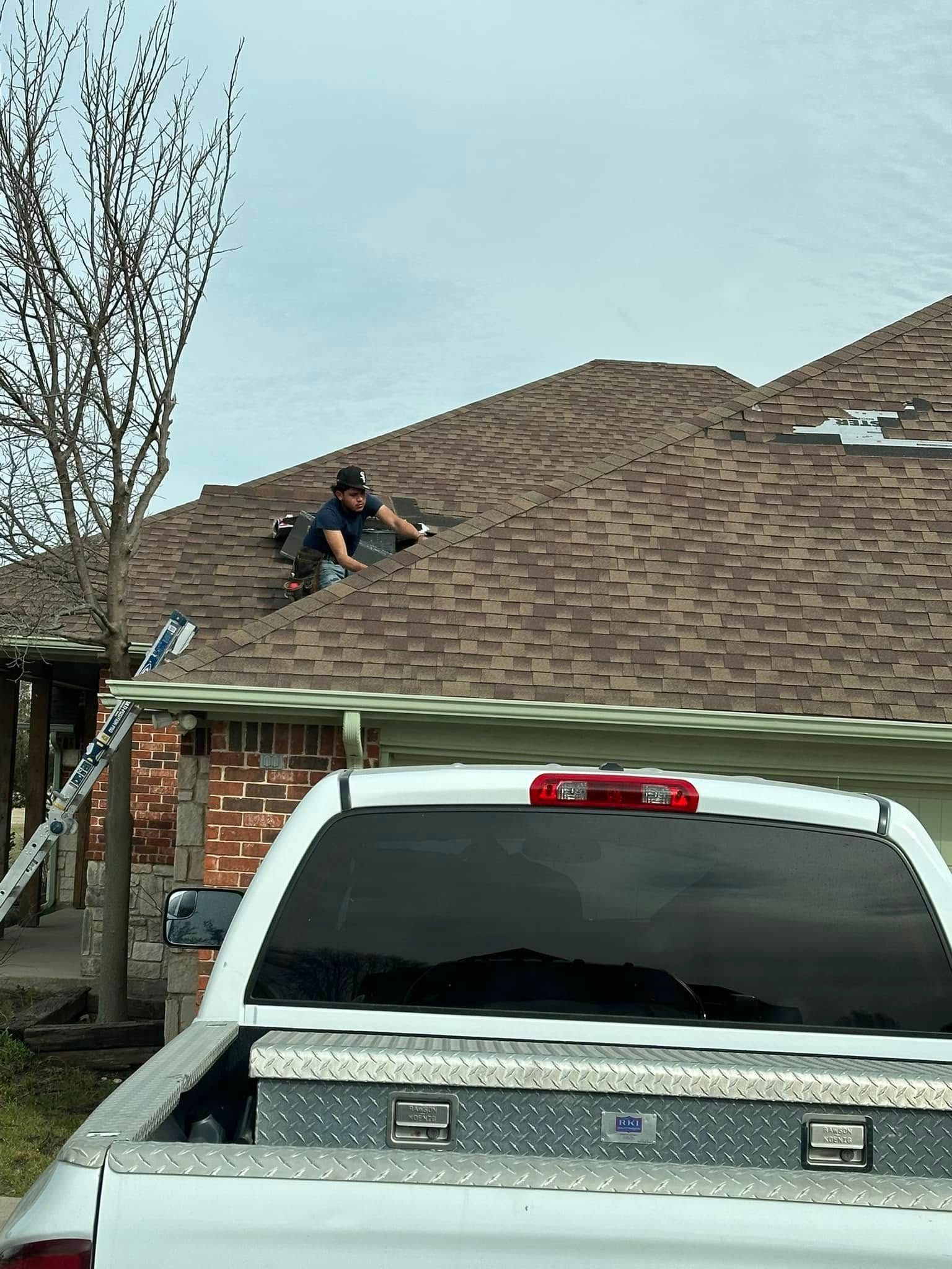 A person on a brown shingle roof working. A white pickup truck parked below.