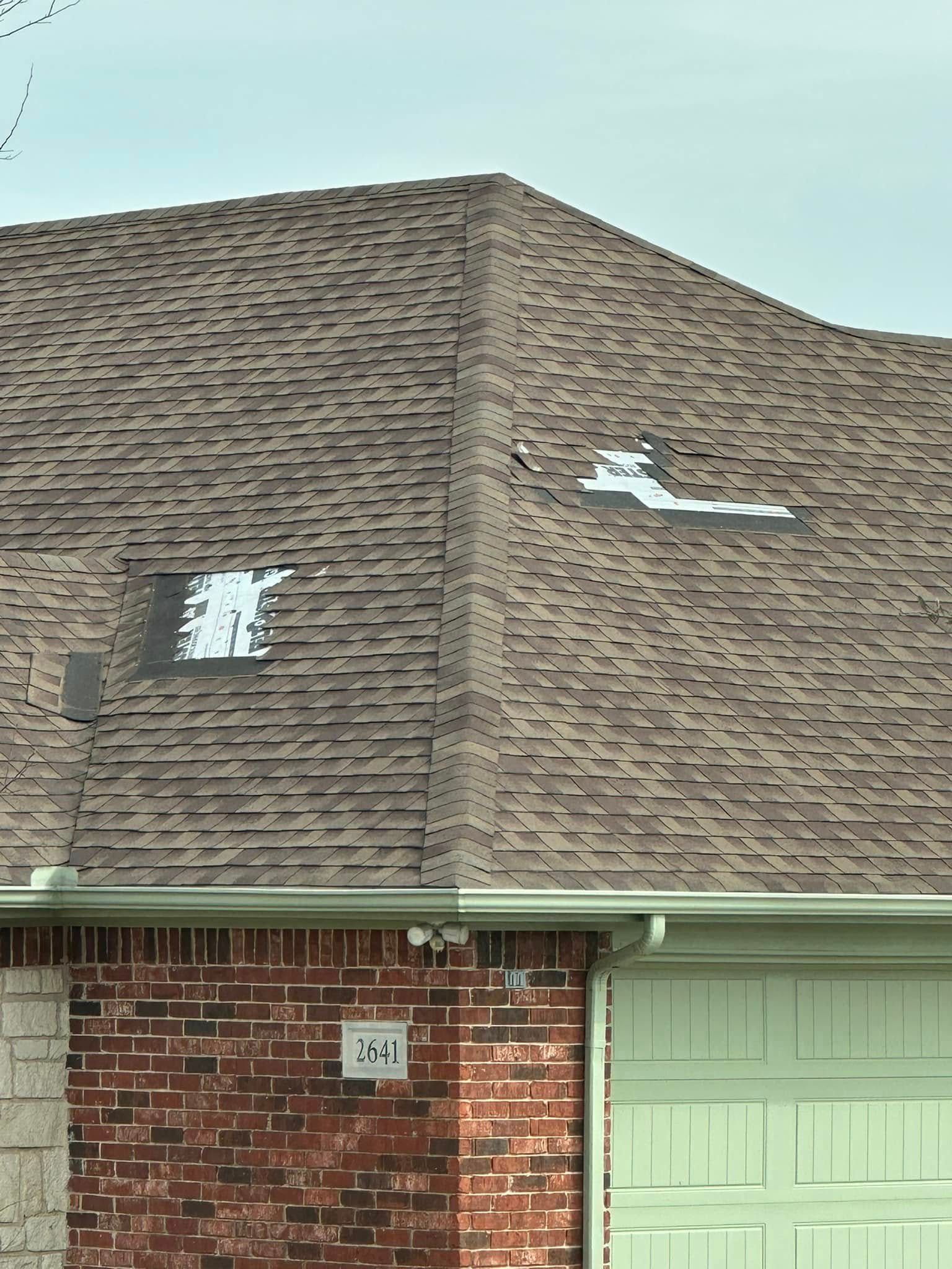 Brown shingle roof with patches of snow, green trim, red brick, and green garage door.