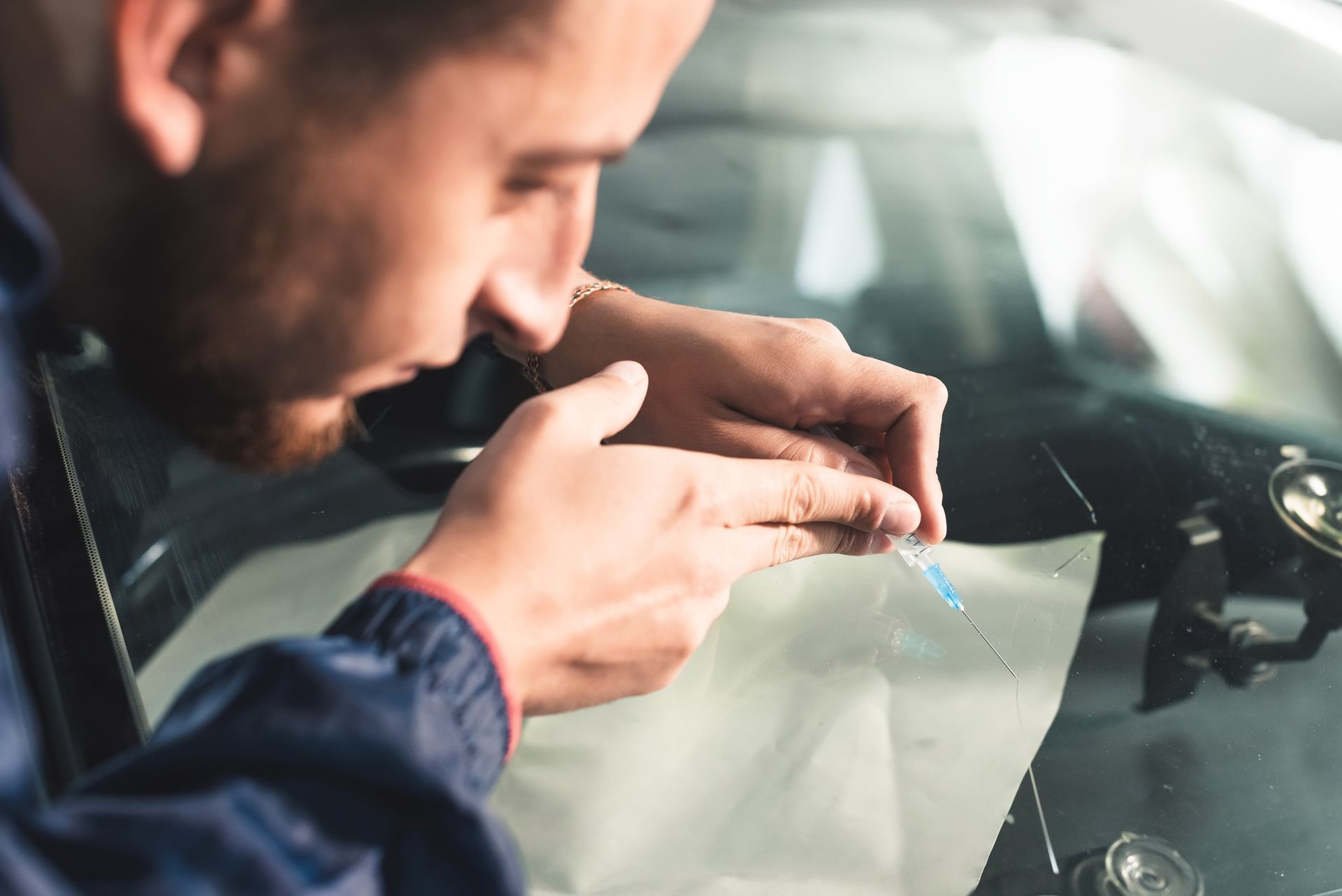 Close-up of a windshield repairman filling a crack in the glass with a special polymer through a syringe. Close-up of a windshield repairman filling a crack in the glass with a special polymer through a syringe.