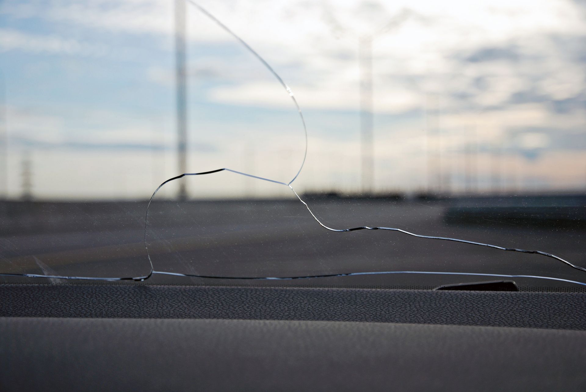 Cracks on car windshield glass. View from inside against empty freeway.