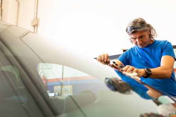 Auto glass mechanic in blue shirt looks at a windshield of a car after repairing it.