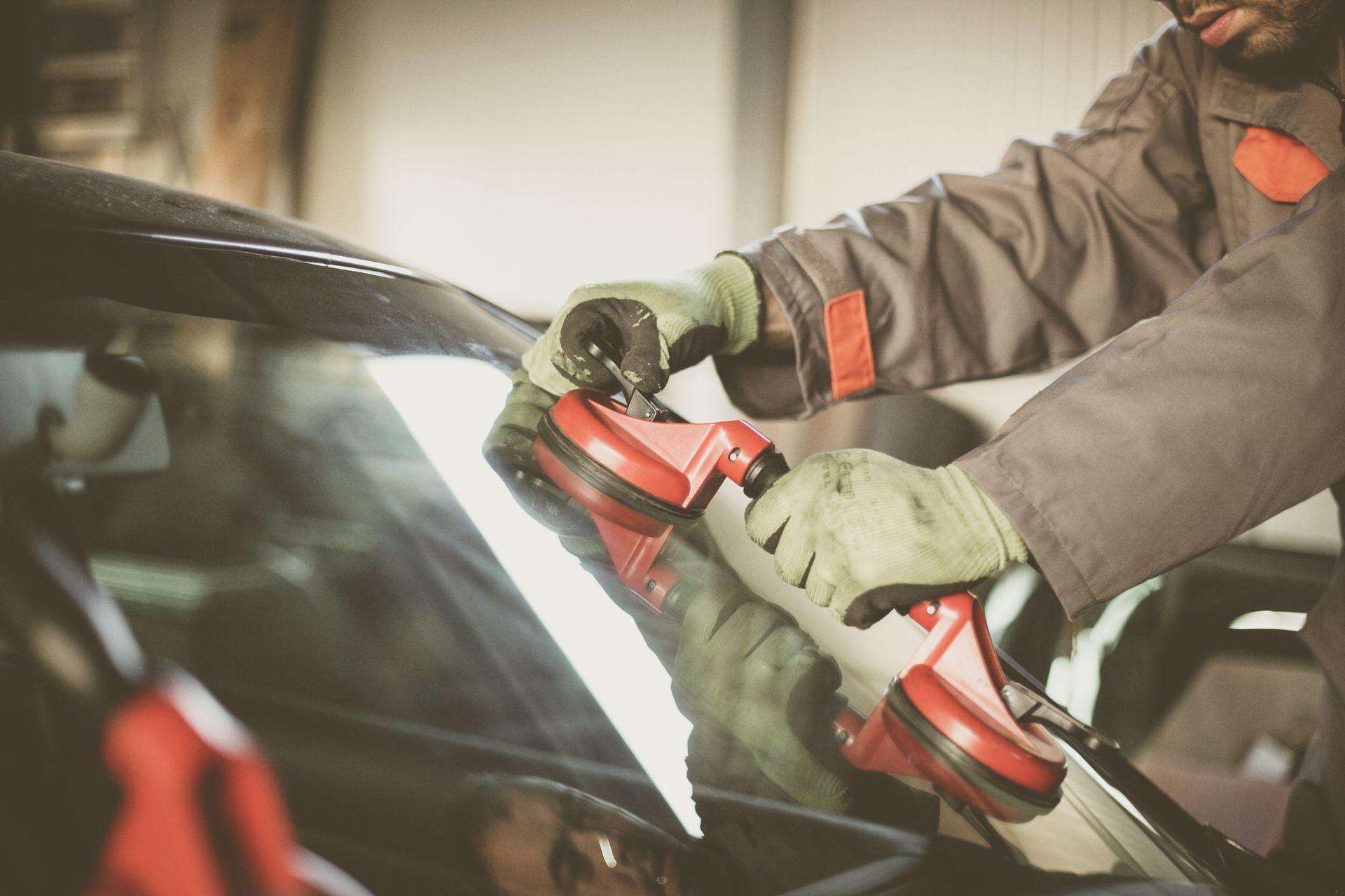Technician replacing windshield with suction tools at local auto glass shop service center.