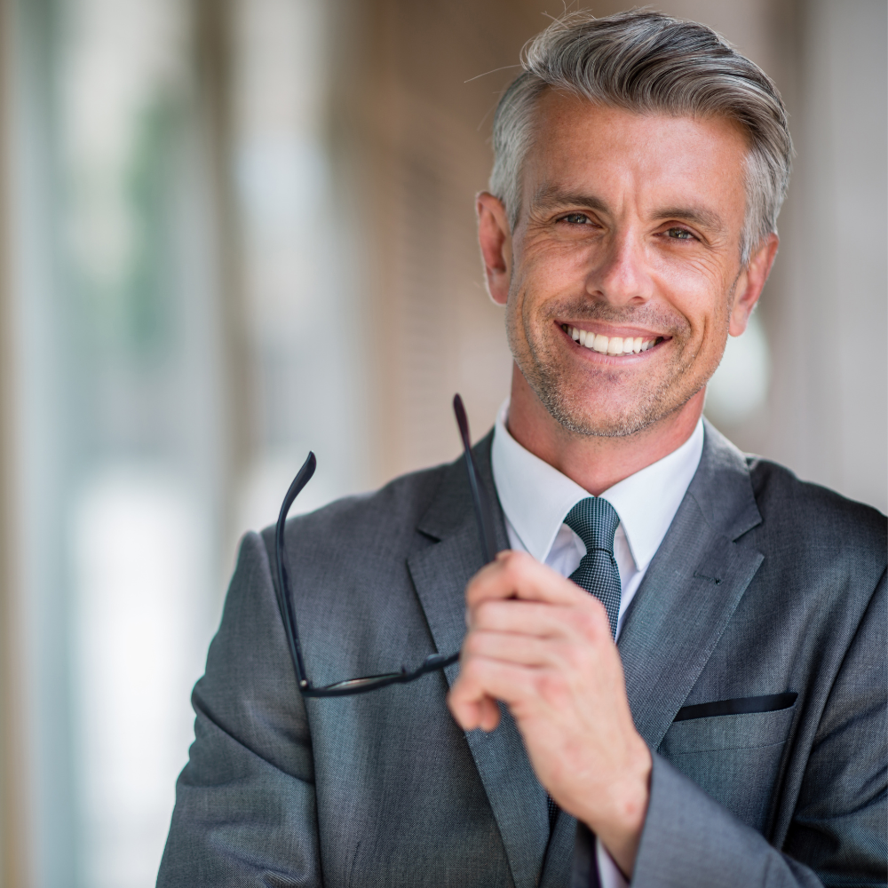 A man in a suit and tie is holding a pair of glasses and smiling.