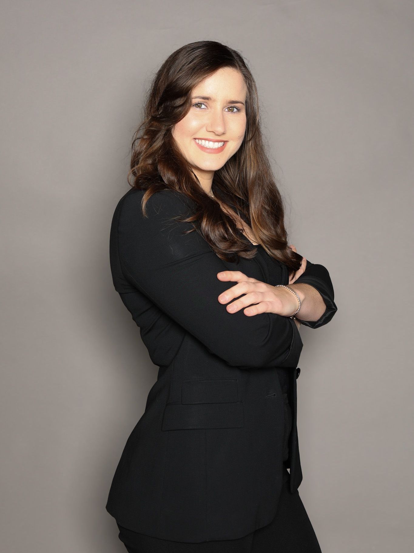 A woman in a black jacket is standing with her arms crossed and smiling.
