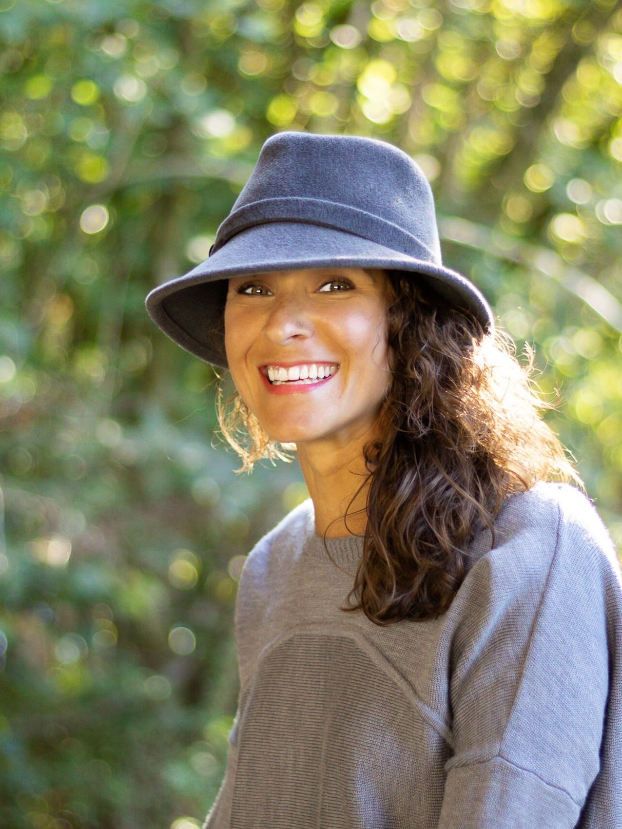 A woman wearing a hat and a sweater is smiling.