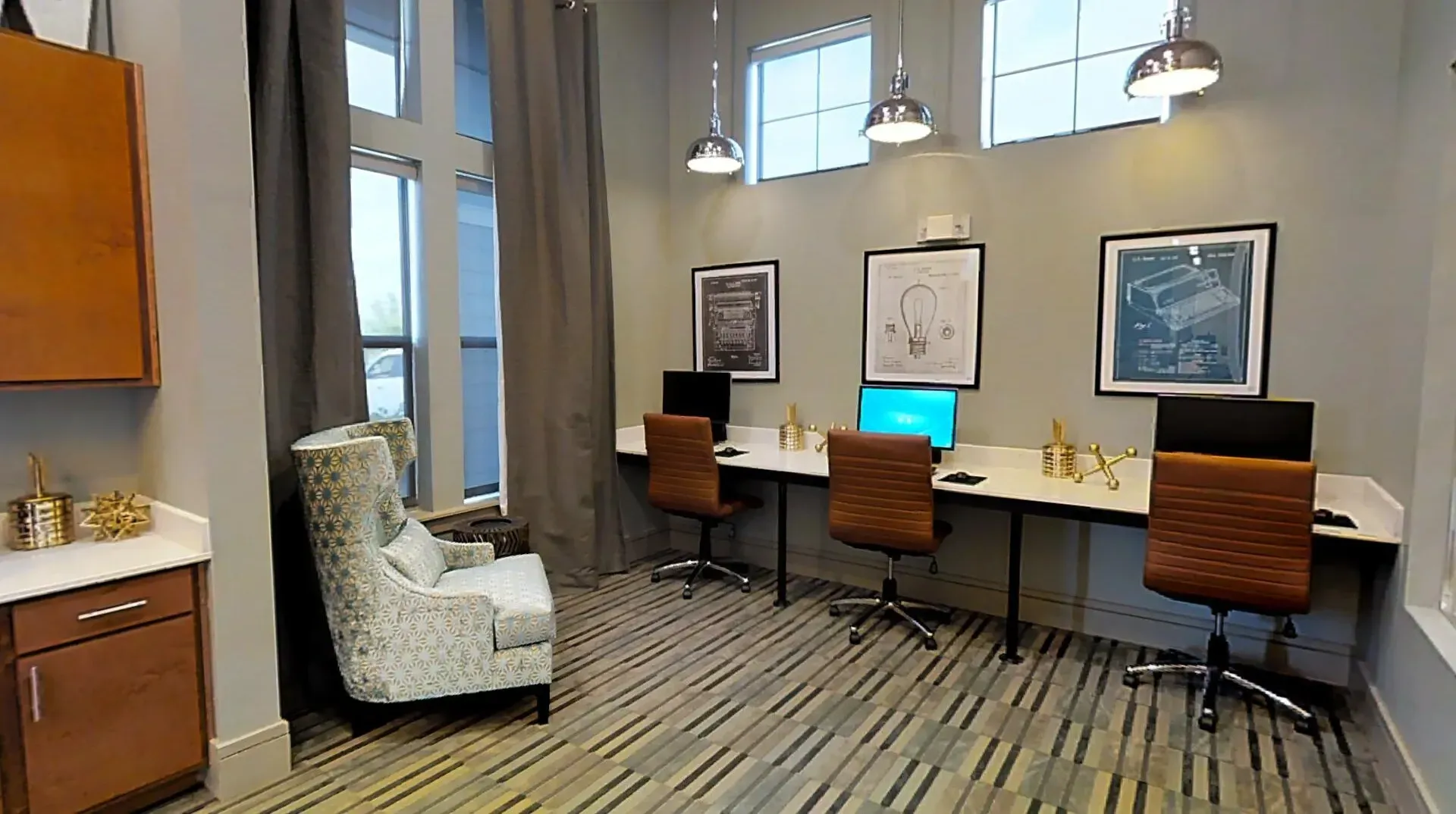 Office-style community workspace with three desks, computers, and framed wall art.