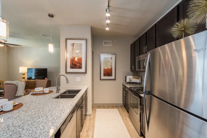 A modern kitchen with granite countertops, stainless steel appliances, dark cabinets, and a kitchen island with sink.