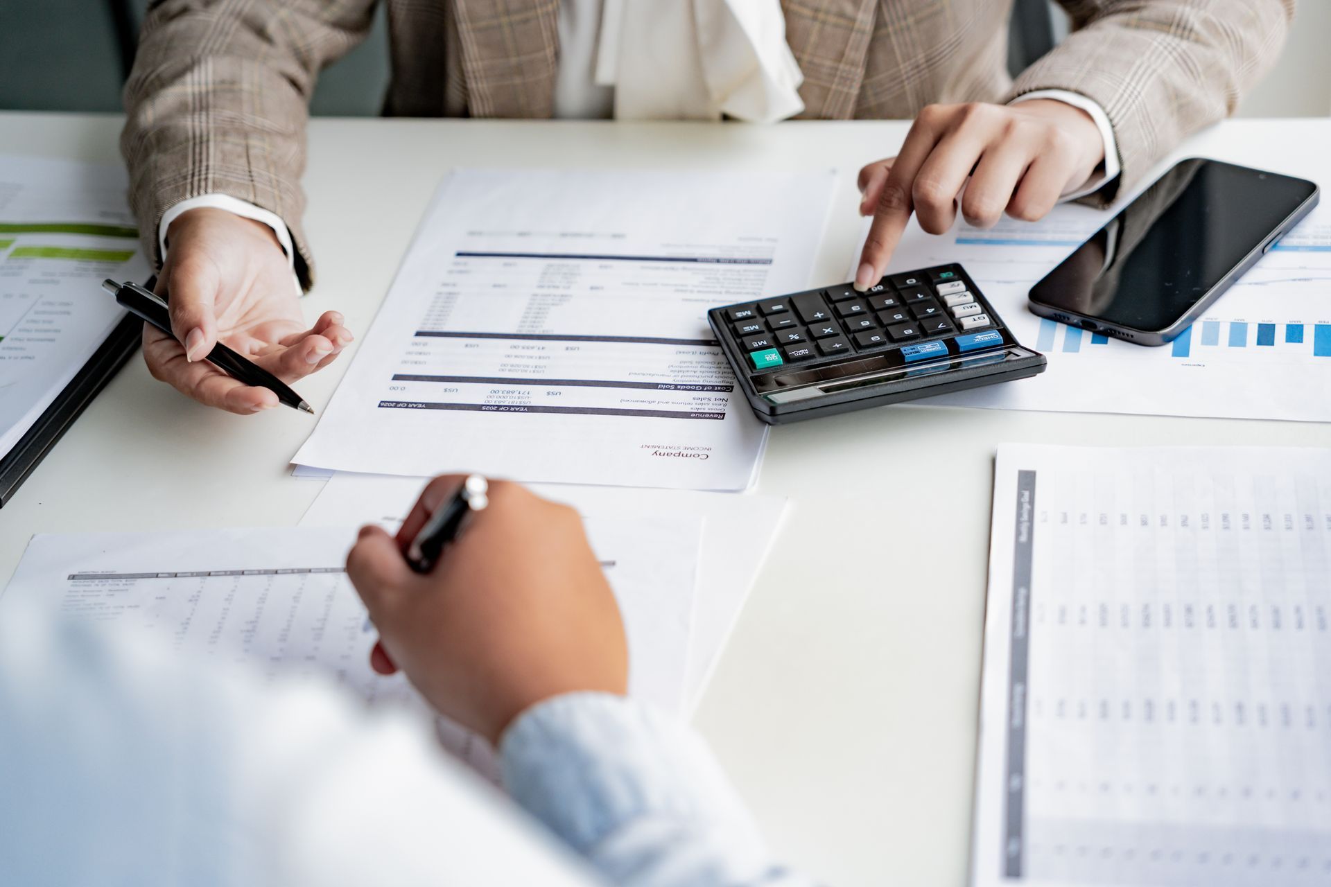 Two people review financial documents on a desk with a calculator and smartphone.