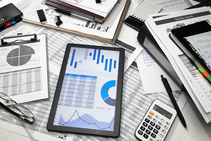 A high-angle view of a desk with a tablet displaying business charts, a calculator, documents, and various office supplies.