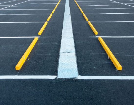 A symmetrical view of an empty parking lot with yellow wheel stops flanking a central painted white divider.