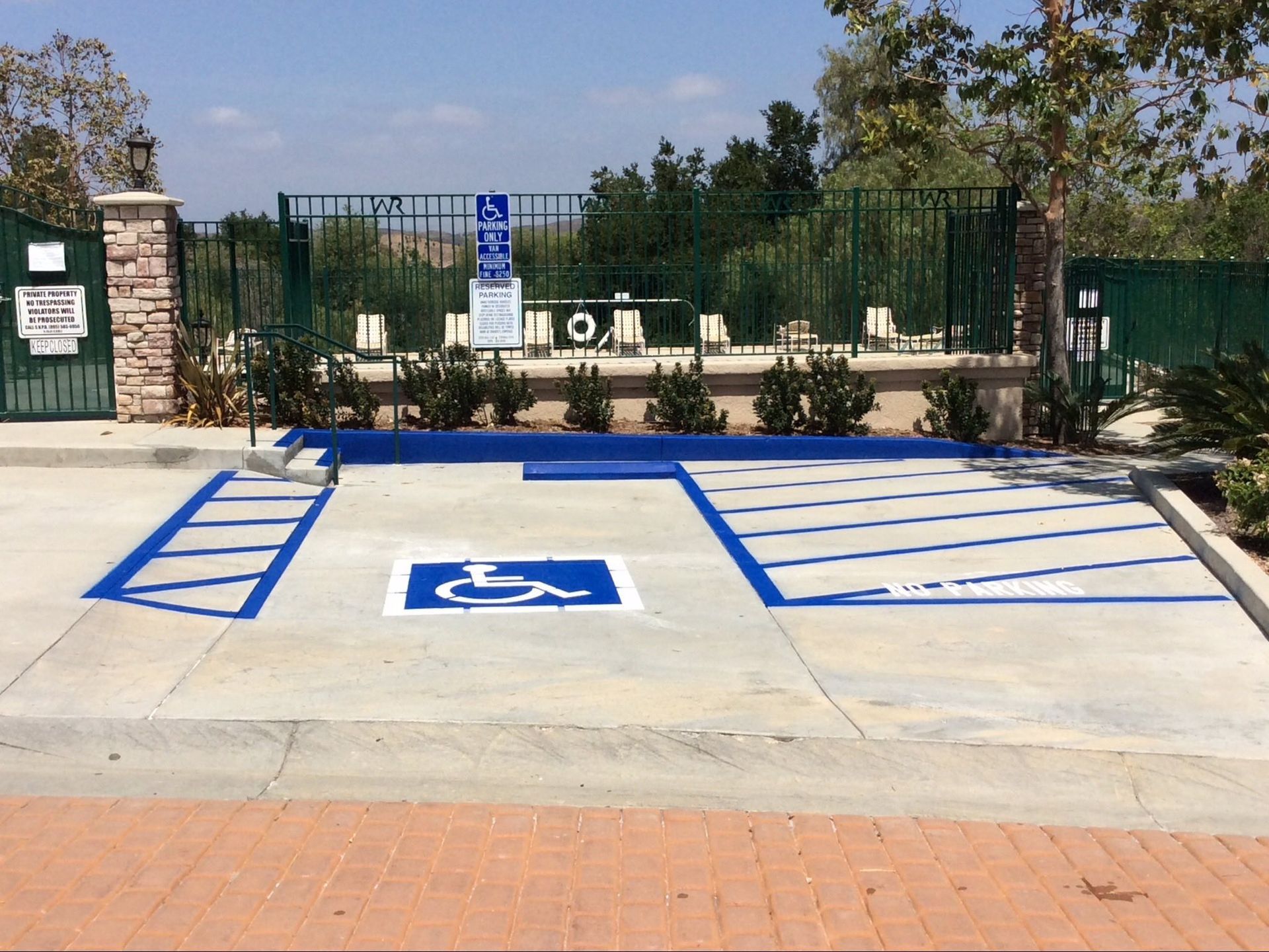 A blue-painted handicap parking space with white access aisles and a wheelchair symbol, located outside a fenced pool area.