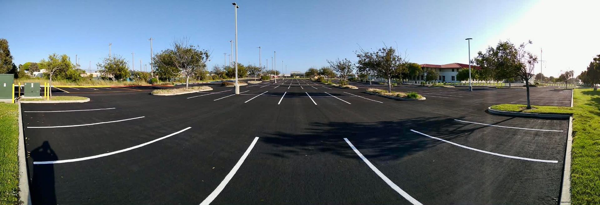 A freshly paved, empty parking lot with bright white painted parking spaces under a clear blue sky.