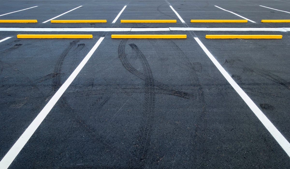 An empty parking lot with marked asphalt spaces and yellow concrete wheel stops.