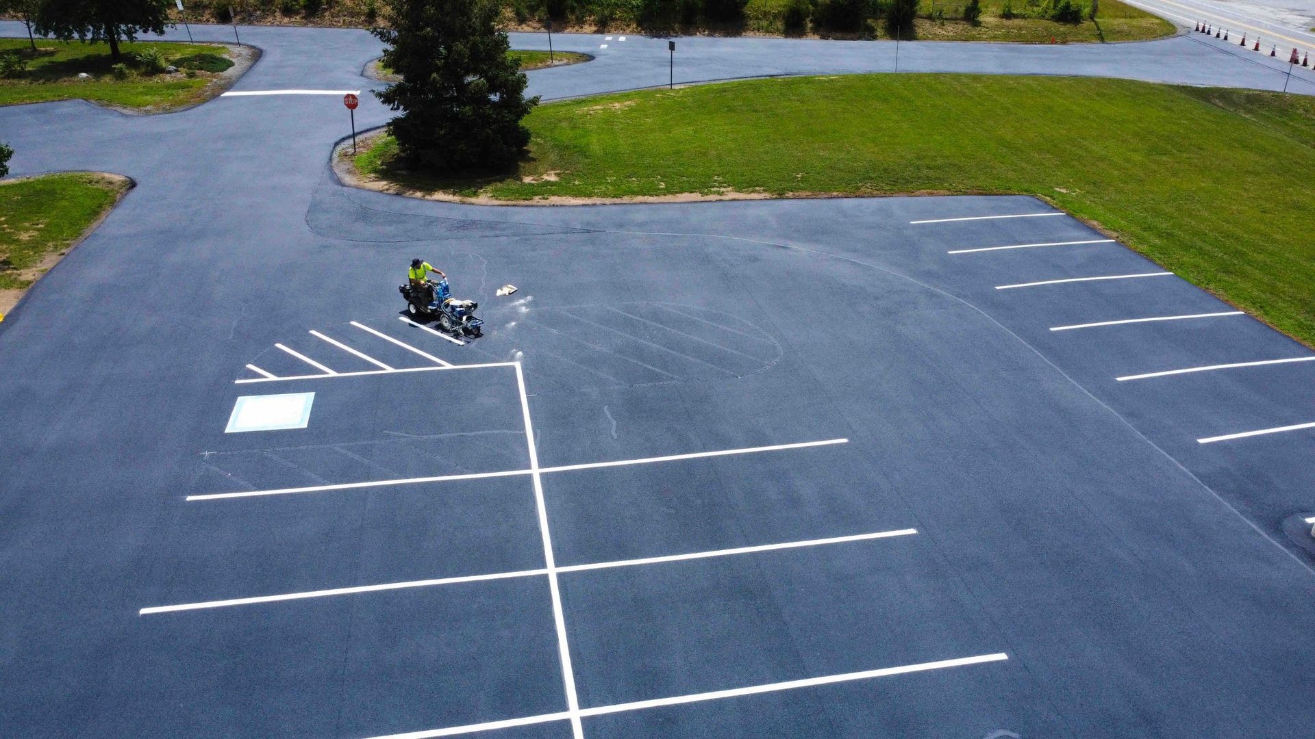 An aerial view of a person riding a motorcycle through a newly paved parking lot with painted white parking lines.