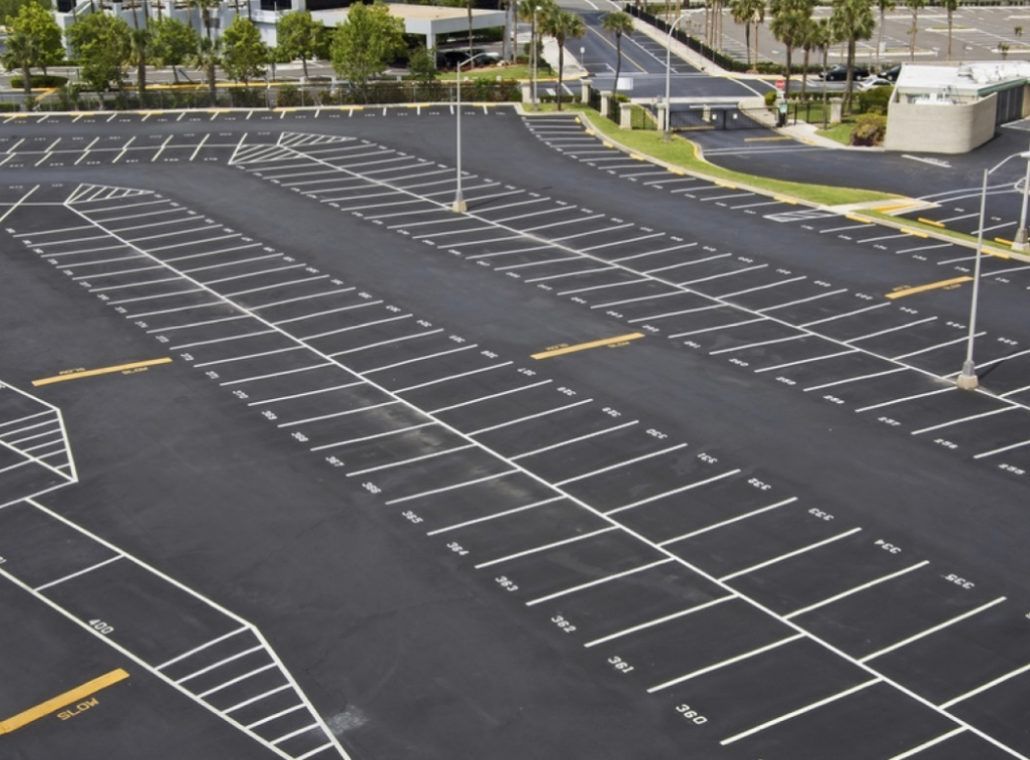 An empty outdoor asphalt parking lot with white painted lines delineating numerous rectangular parking spaces.