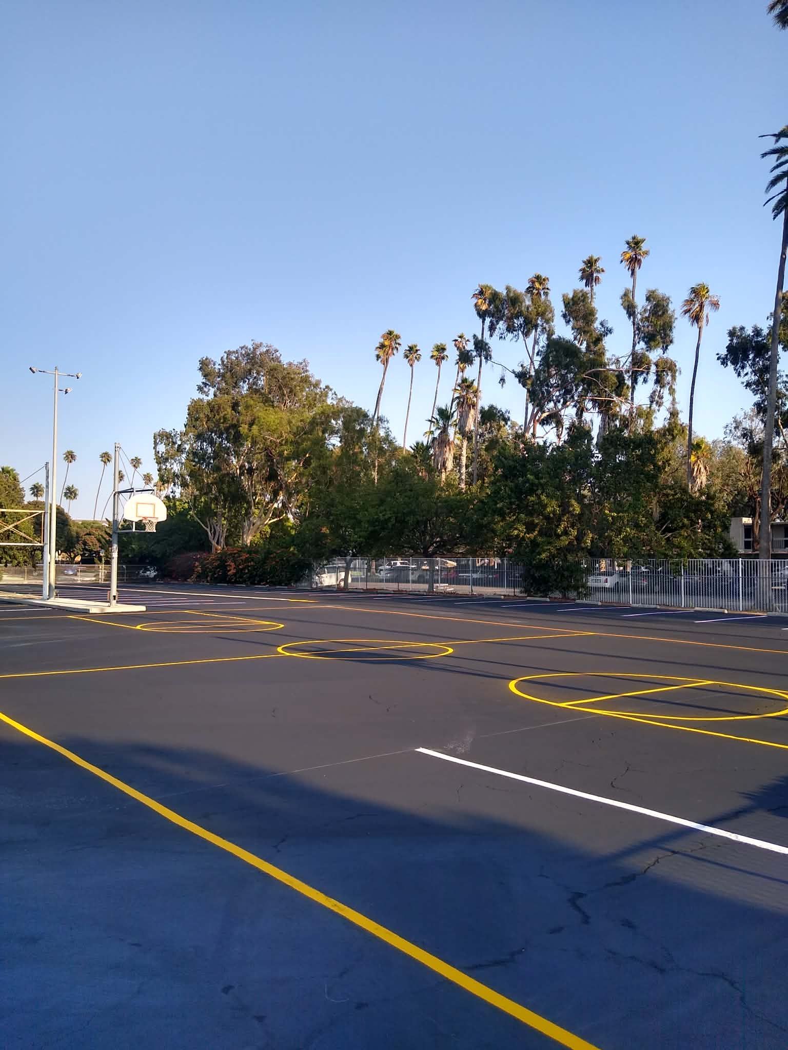 A striping machine paints white lines on a freshly paved asphalt parking lot with numbered stalls.