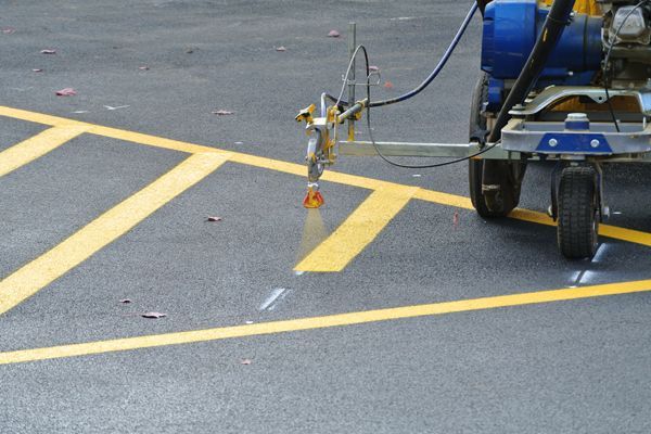 A mechanical striper sprays yellow paint onto asphalt to mark lines in a parking lot.