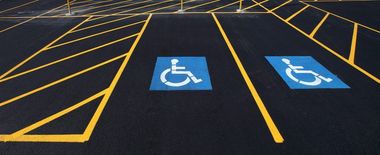 Two designated blue and white wheelchair-accessible parking spaces on black asphalt marked with yellow safety stripes.