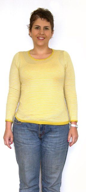 Una mujer que viste una camisa de rayas amarillas y pantalones vaqueros azules está parada frente a un fondo blanco.