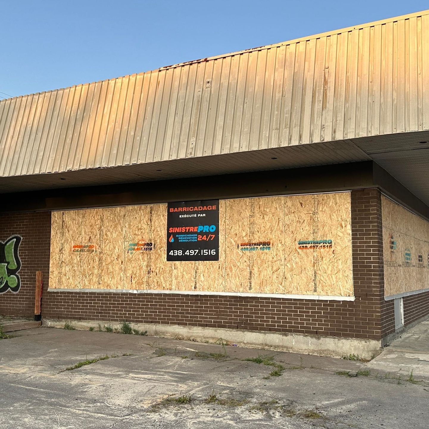 Bâtiment barricadé avec des fenêtres recouvertes de contreplaqué, des graffitis et un panneau à vendre.