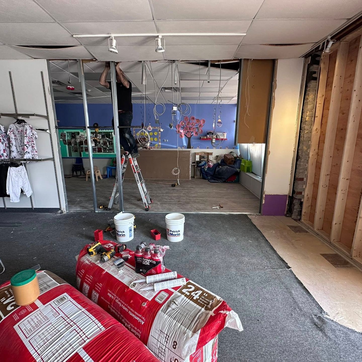 Une personne sur une échelle travaille à la rénovation intérieure d'un magasin, avec des murs, des outils et des matériaux exposés.