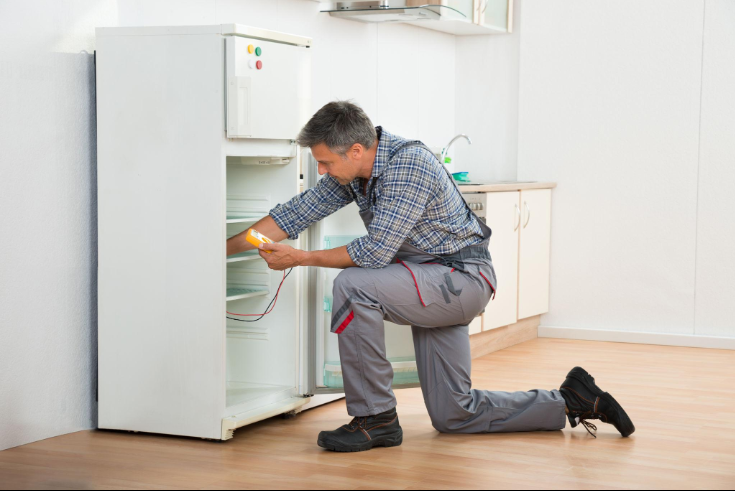 “Repair technician kneeling beside a refrigerator and checking the lower compartment during an appliance repair service in Millcreek, UT”