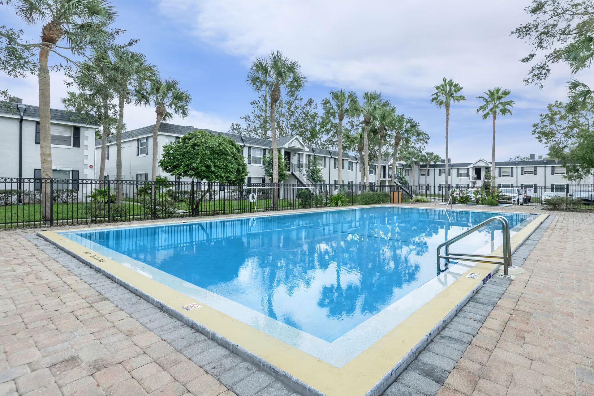 A large swimming pool is surrounded by palm trees and buildings.