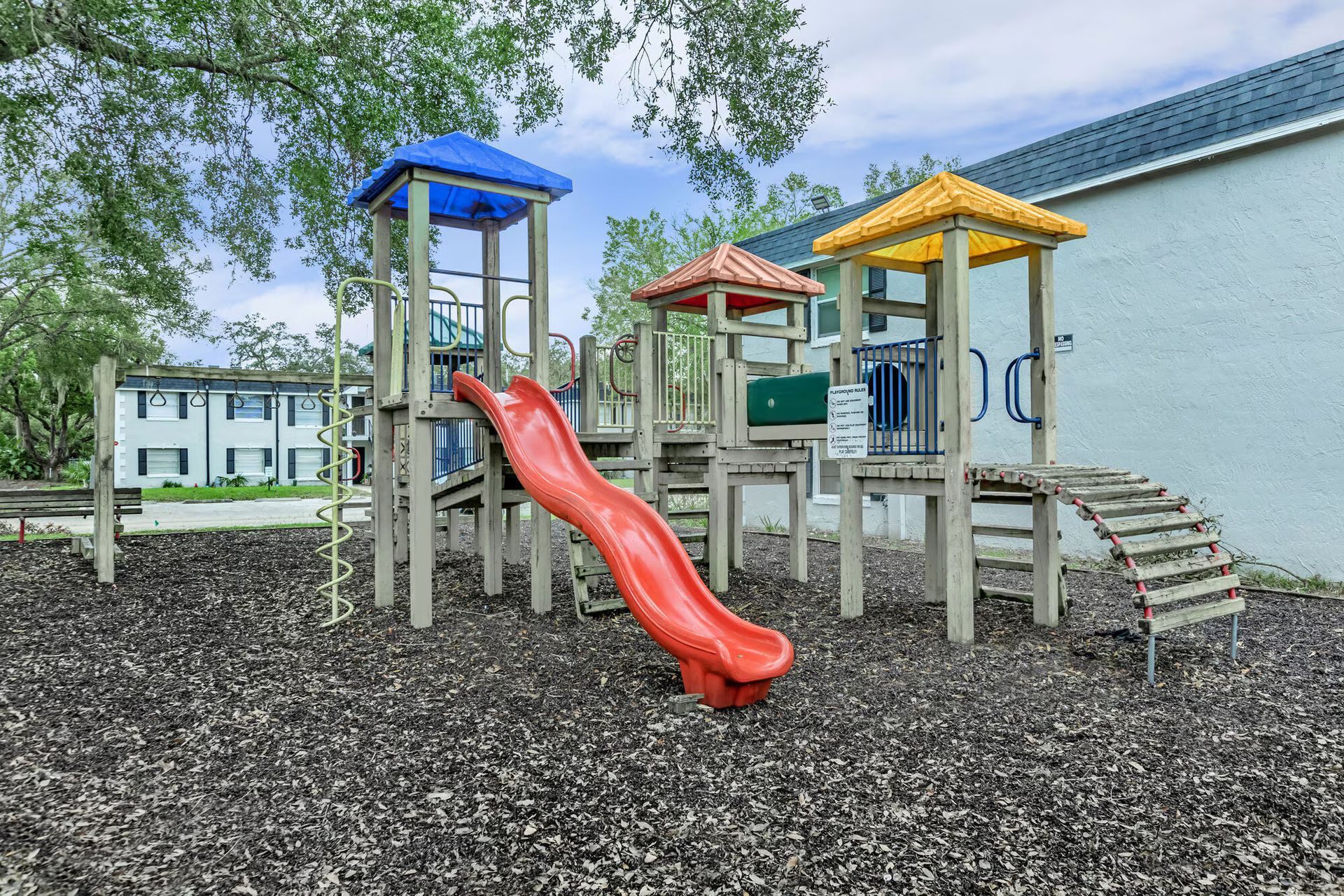 A playground with a red slide and a blue tower in front of a building.