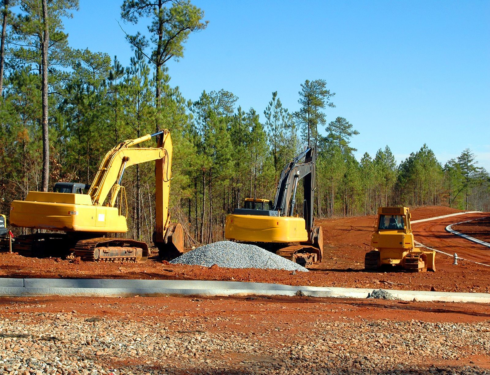 Two yellow excavators are working on a dirt road