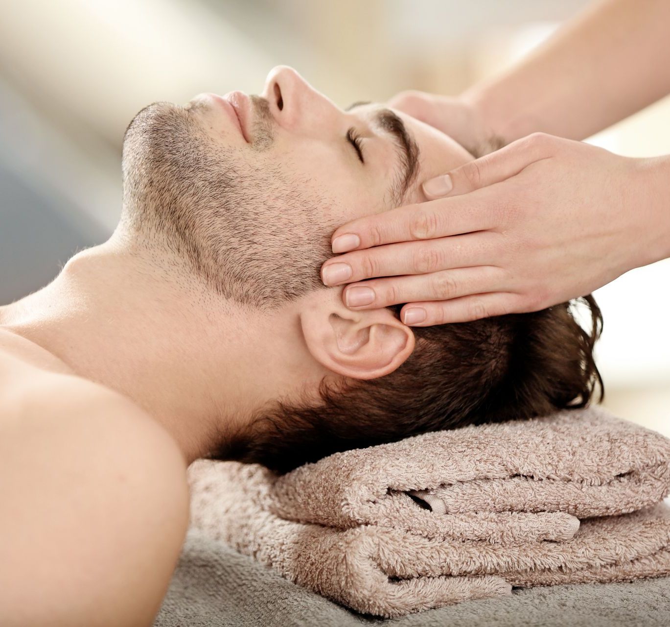 Ein Mann liegt auf einem Handtuch und bekommt eine Kopfmassage.