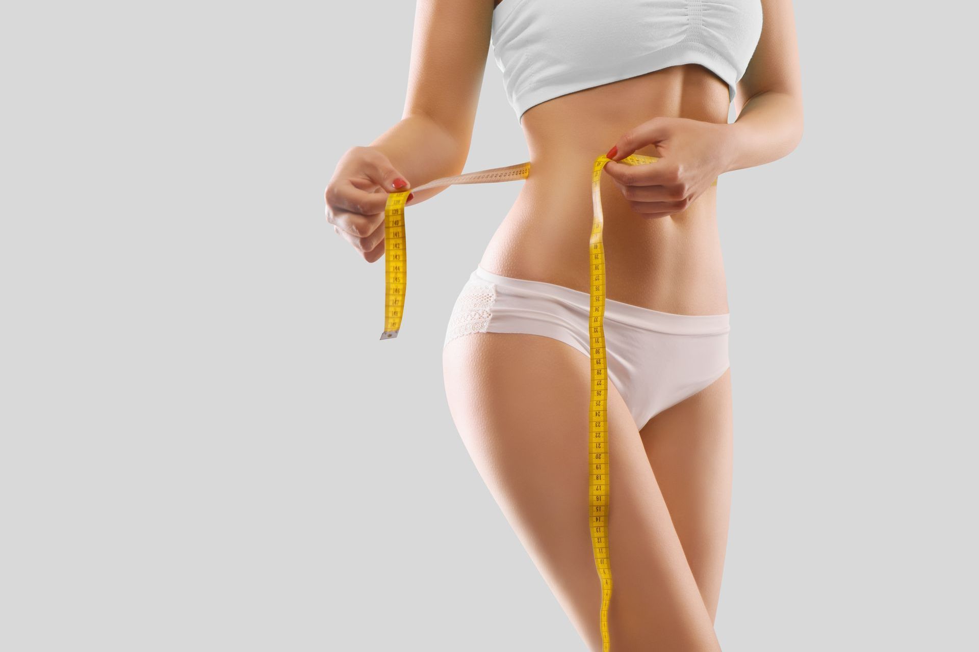 Eine Frau misst ihre Taille mit einem Maßband.