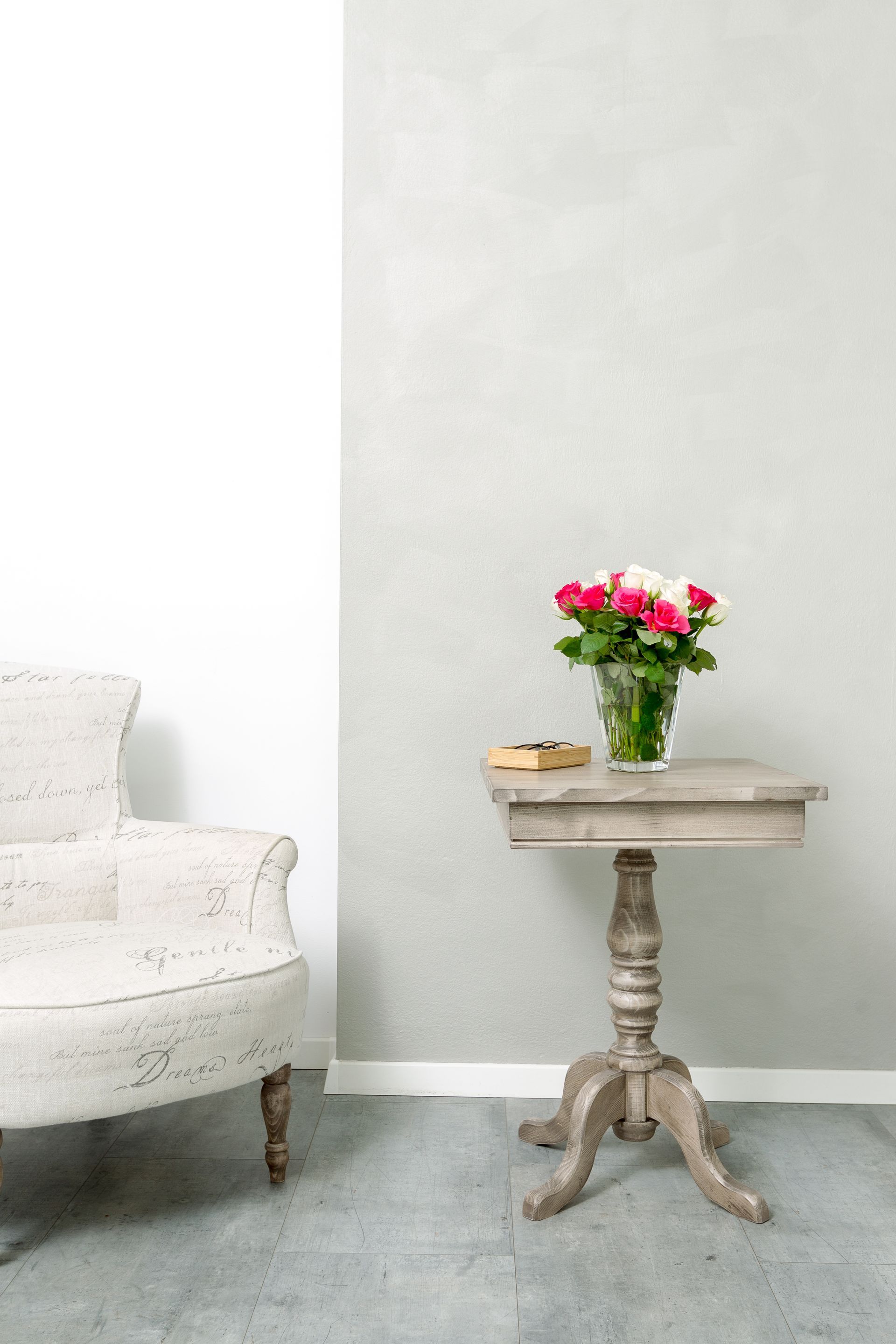 Ein Tisch mit einer Blumenvase darauf in einem Wohnzimmer neben einem Stuhl.