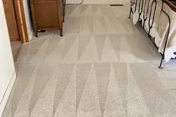 Clean, patterned carpet in a room with a bed and dresser. The pattern is geometric with pointed triangles.