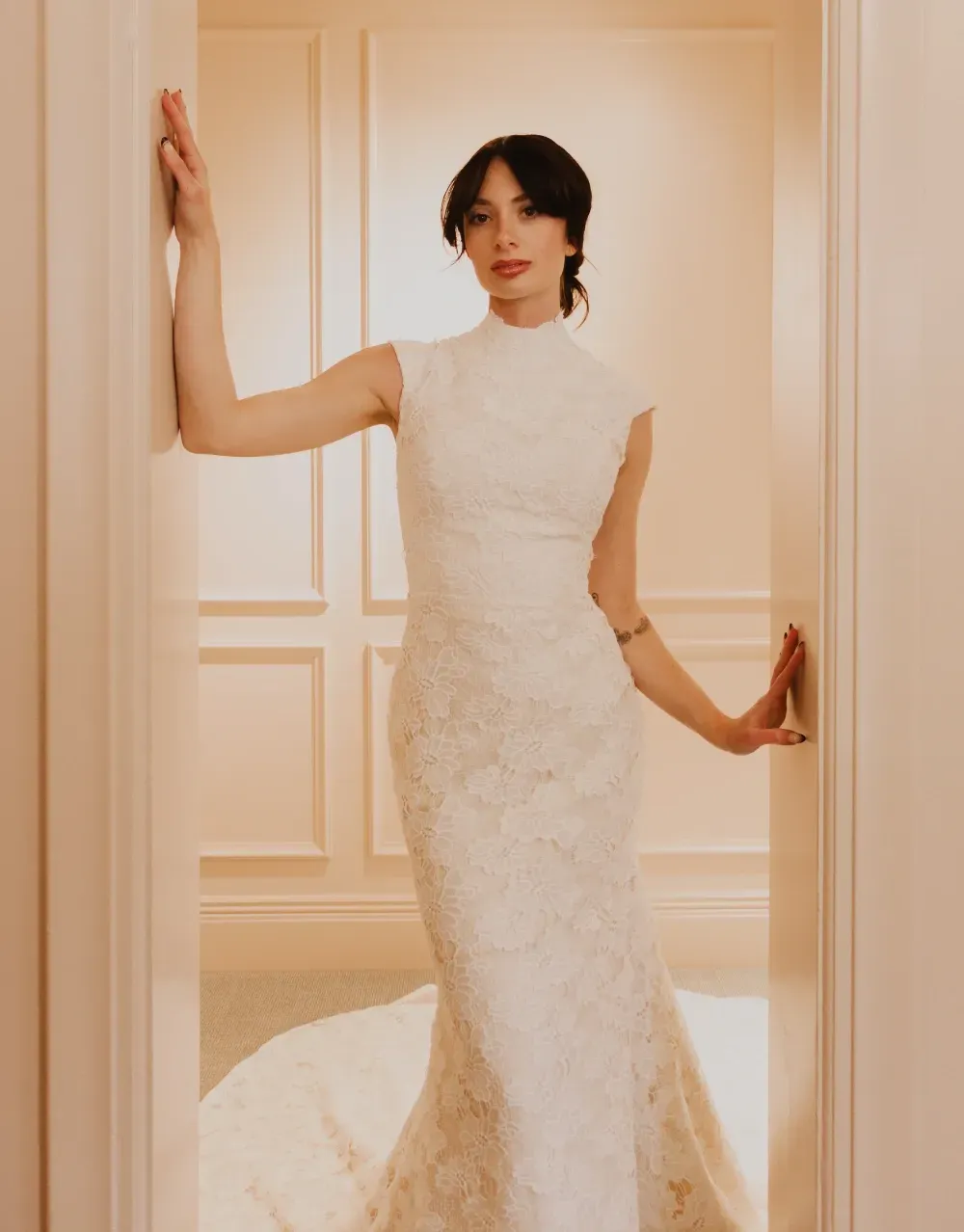 Woman in white lace dress, leaning against a doorway, arms outstretched.