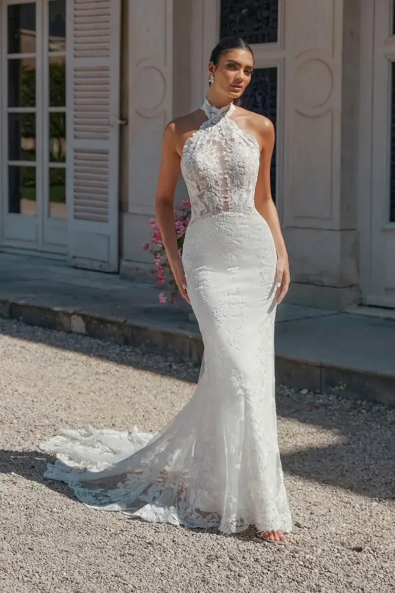 Woman in white bridal gown with high neck, detailed bodice, and mermaid skirt, posing outdoors.